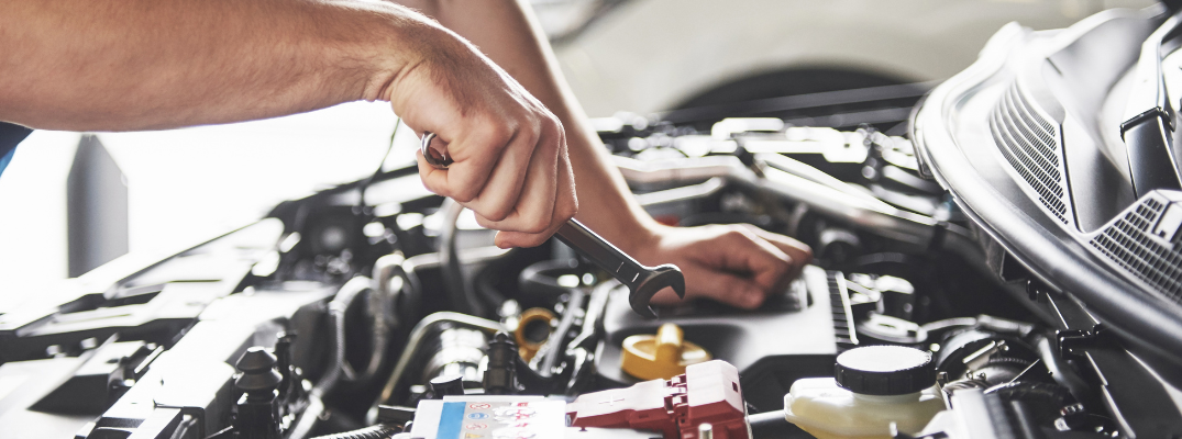 Close up on a technicians' hand using a wrench under the hood of a car
